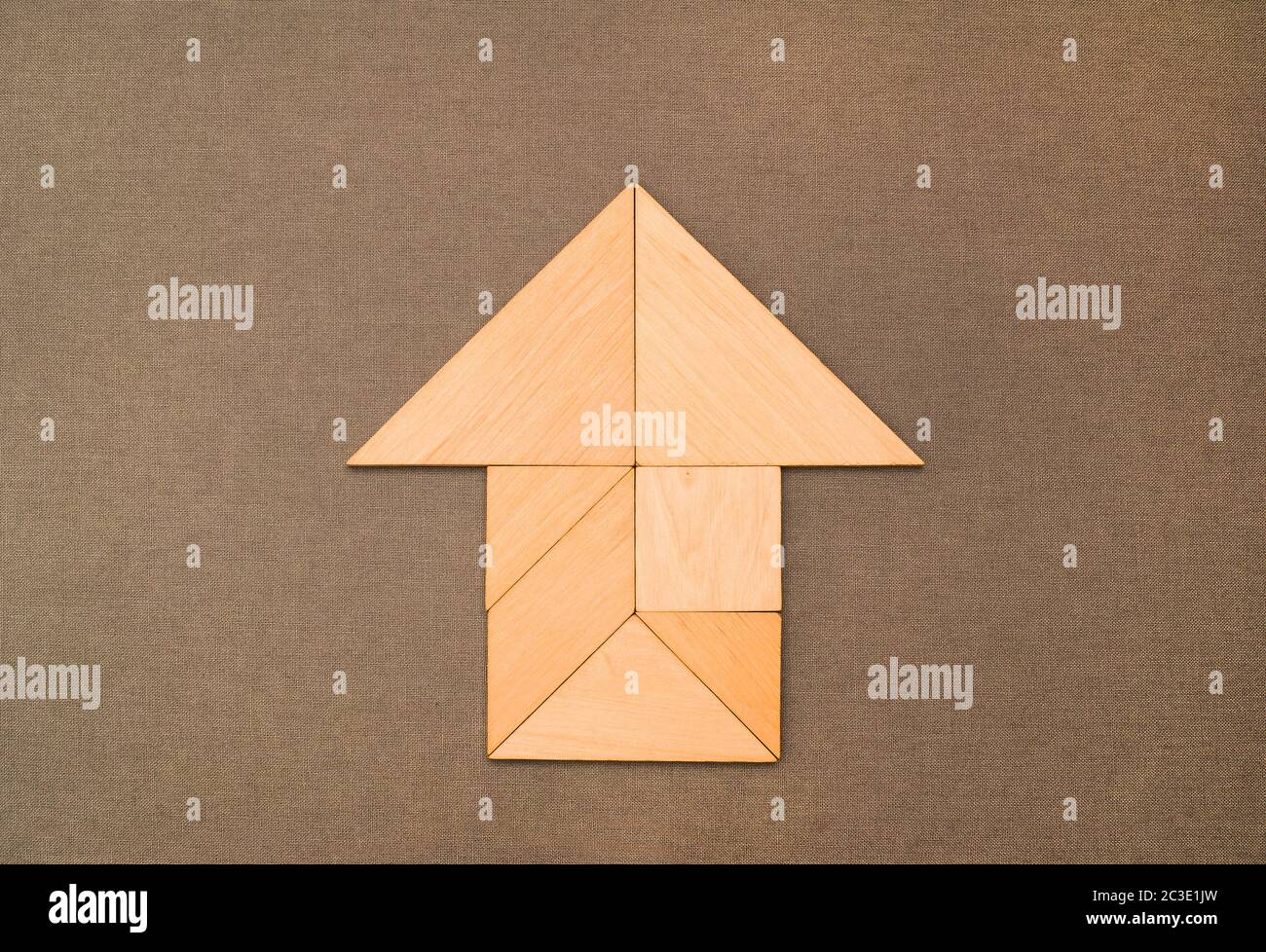 Flat lay - pictogram, symbol, icon of house and arrow made of wooden tangram pieces. Unicolor background made of grey fabric texture. Stock Photo