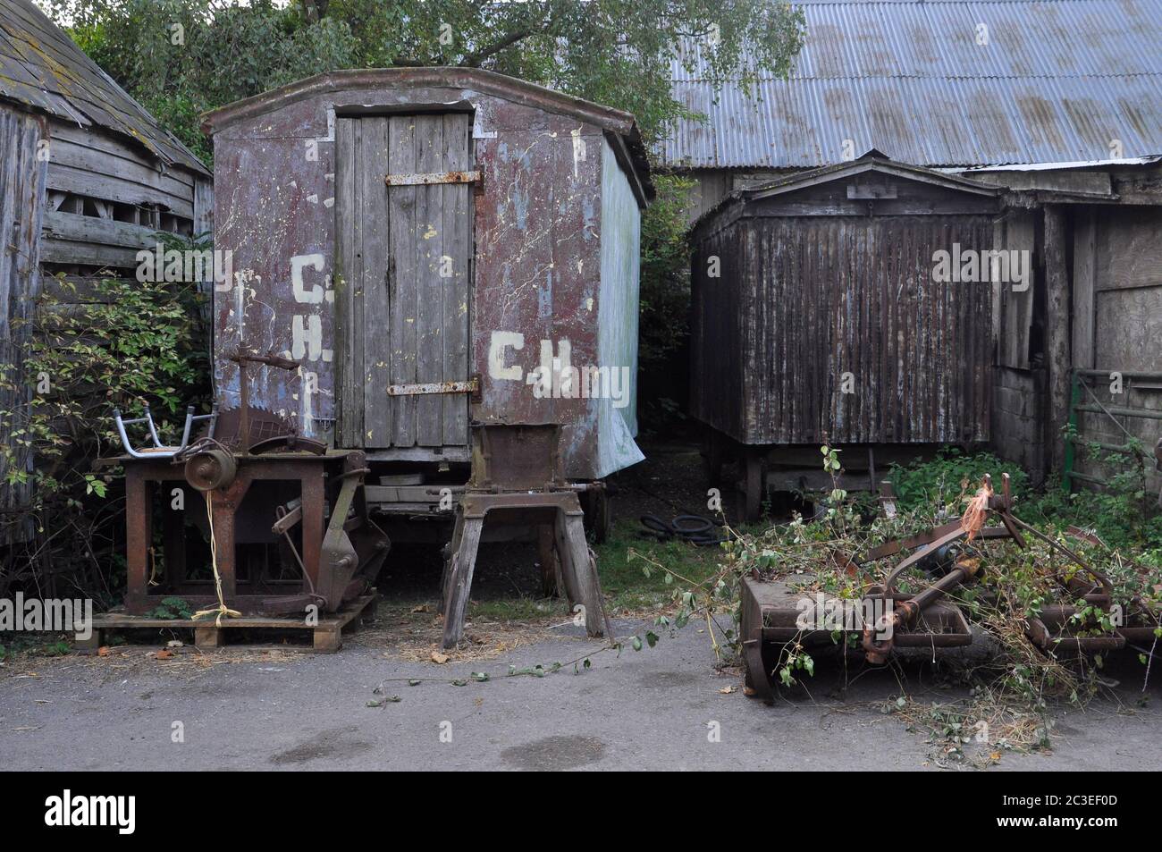 Derelict old wheeled shepherds huts used for storage and old farm machinery in a farm yard at Purbeck in Dorset.UK Stock Photo