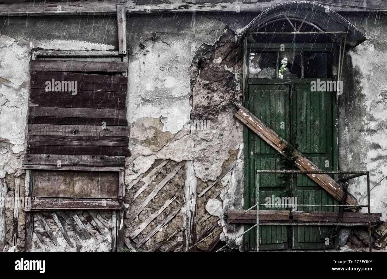 destroyed building with a boarded up window and a door in the rain Stock Photo