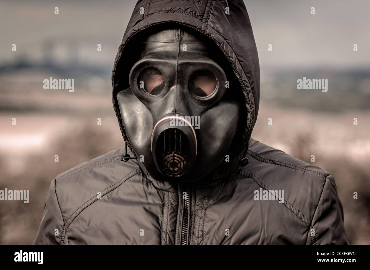 portrait of a man in a gas mask and a hood against the background of smoke from factory pipes close up Stock Photo