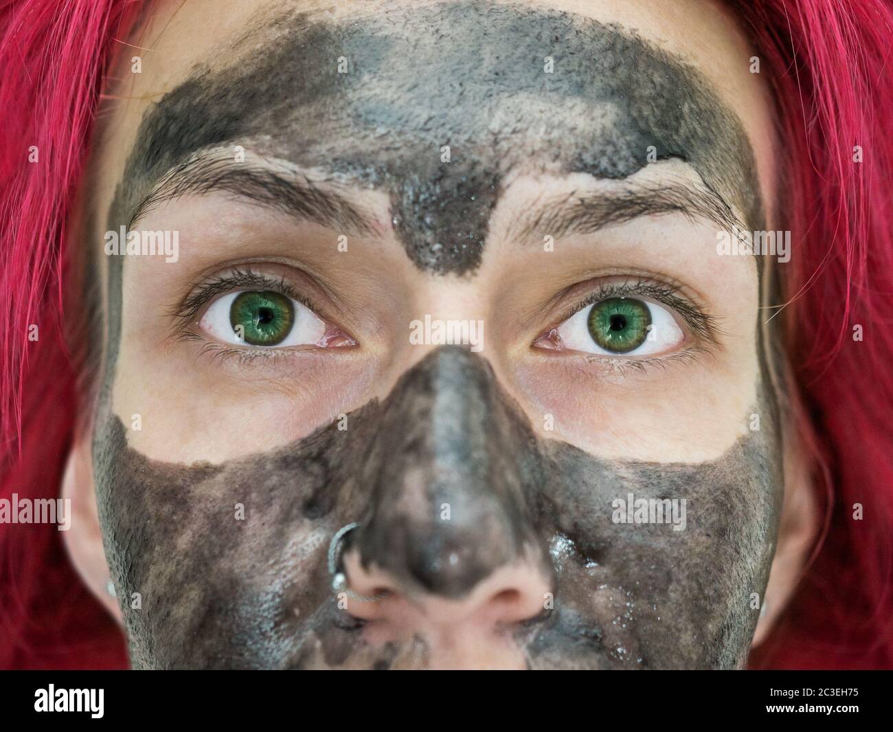 Close-up photo of a fragment of the face of a girl with bright green eyes, red hair and a black peel off mask on her face Stock Photo