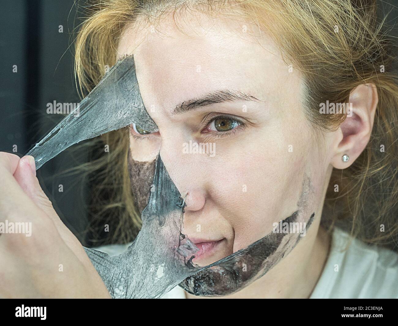 Girl rips off black thin transparent mask to clean pores Stock Photo