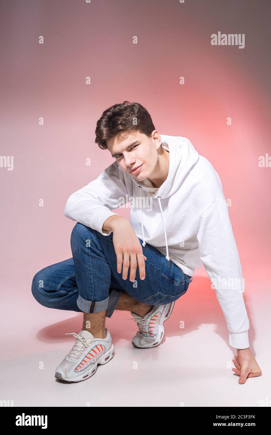 Fashionable handsome young European male model dressed in white sweatshirt,  blue jeans and white sneakers posing in studio on a Stock Photo - Alamy