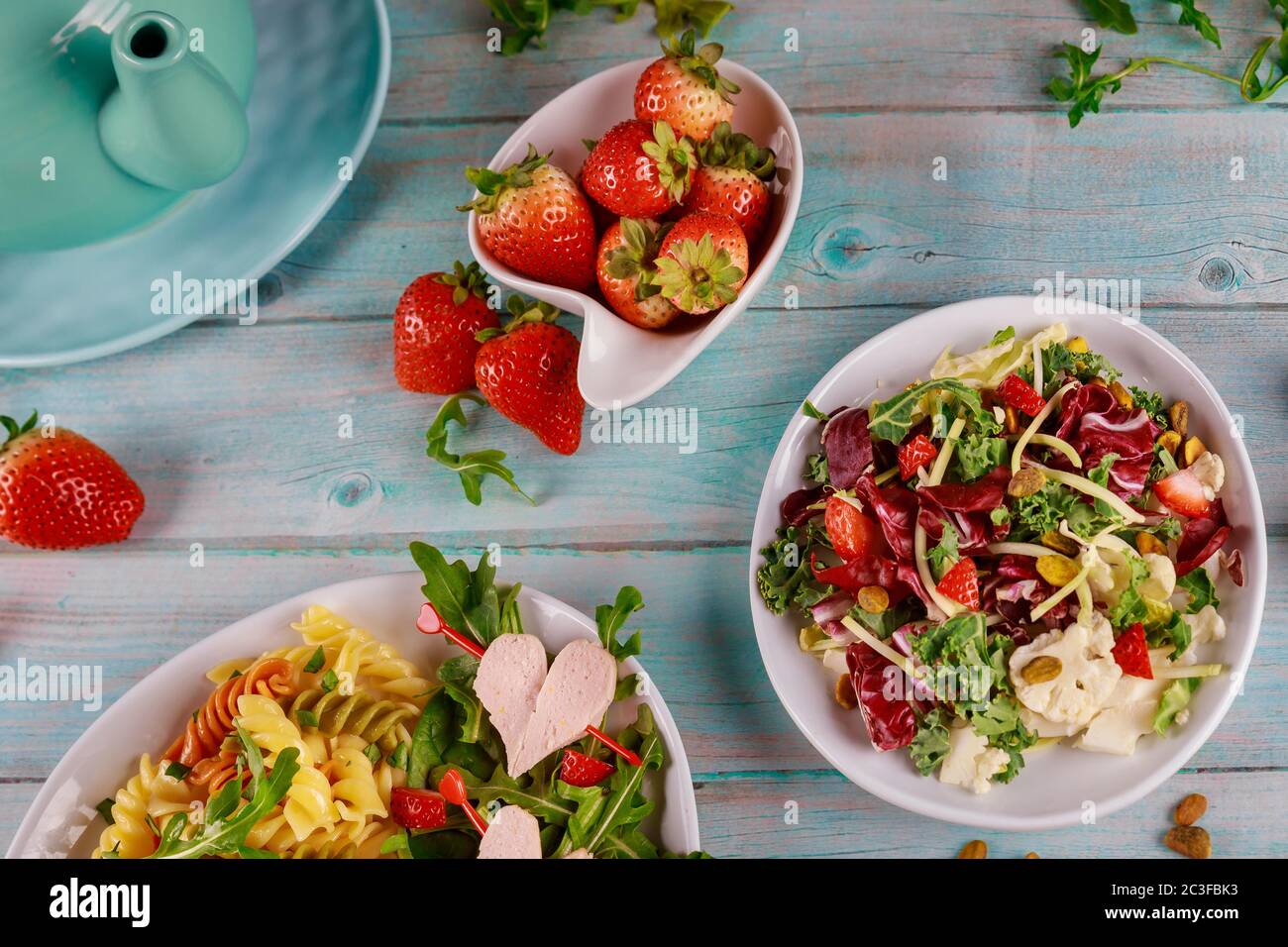 Colorful rotini pasta with healthy spring salad and fresh strawberries on wooden background. Stock Photo
