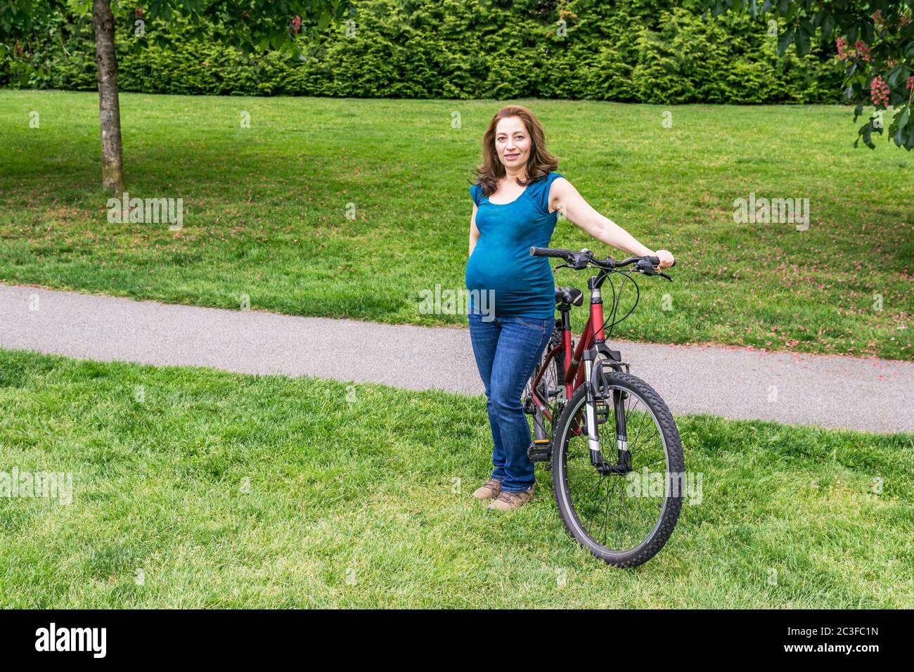 pregnant woman on the green lawn in a park holding bicycle ready to(02)