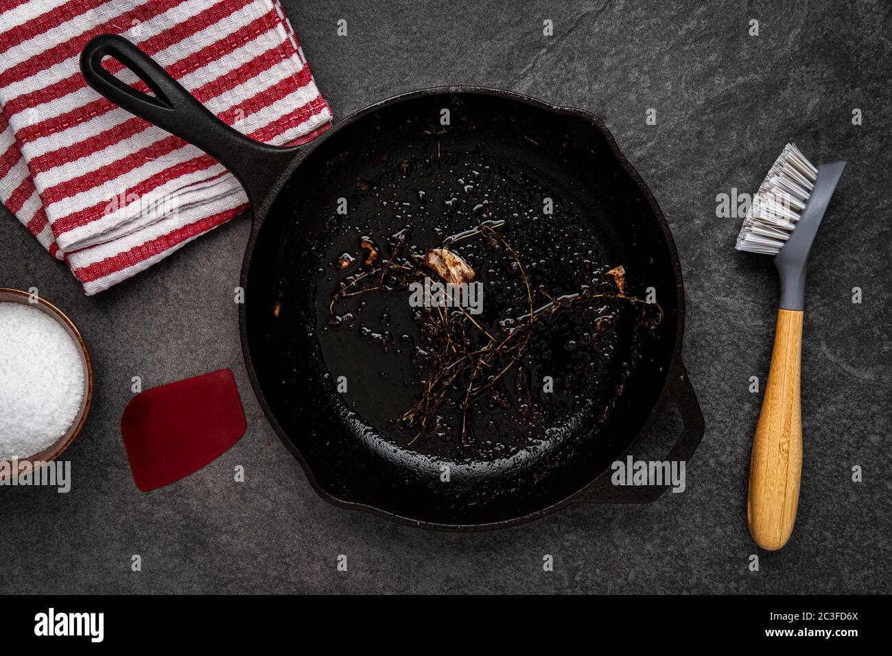 Dirty cast iron skillet being prepared for cleaning with coarse salt, brush,  scraper and dish towel on a counter Stock Photo - Alamy