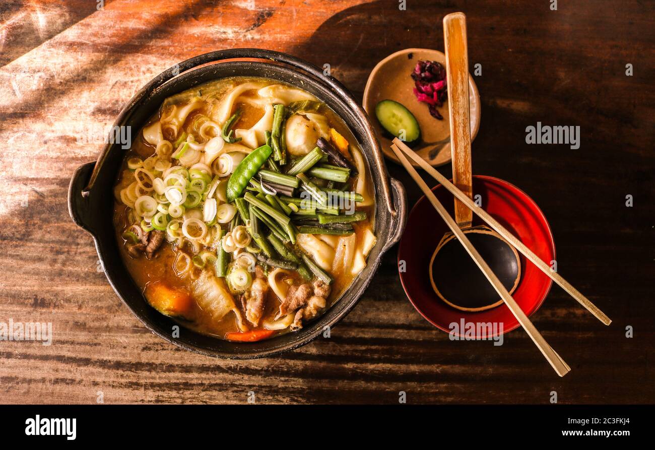Top-down view of a bowl of Japanese houtou noodles and side dishes on a worn wooden tabletop Stock Photo