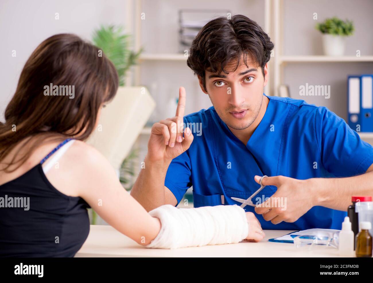 Young woman with bandaged arm visiting male doctor traumotologis Stock