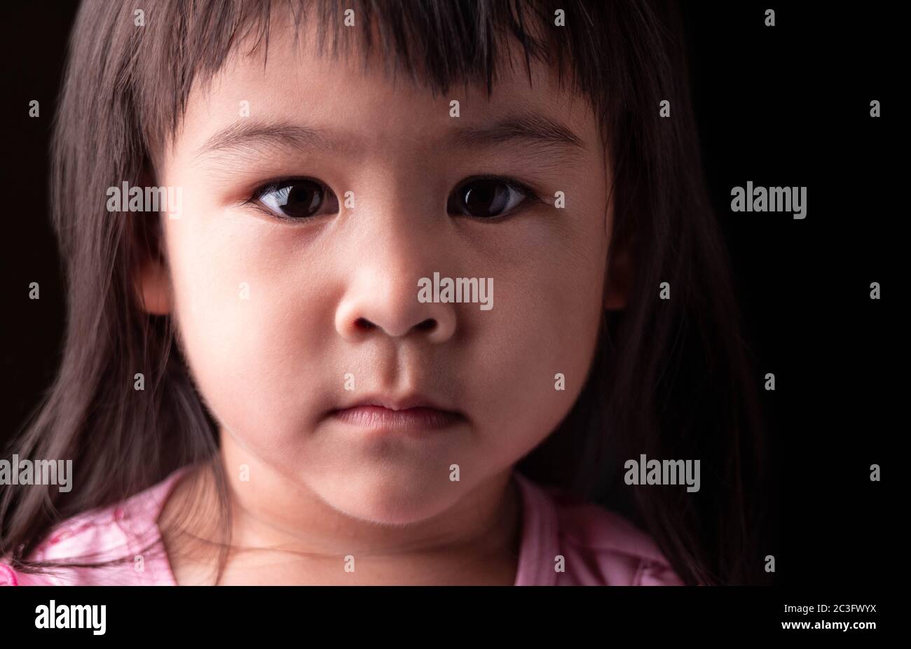 Portrait face of Asian little child girl with confidence expression on dark background. Stock Photo