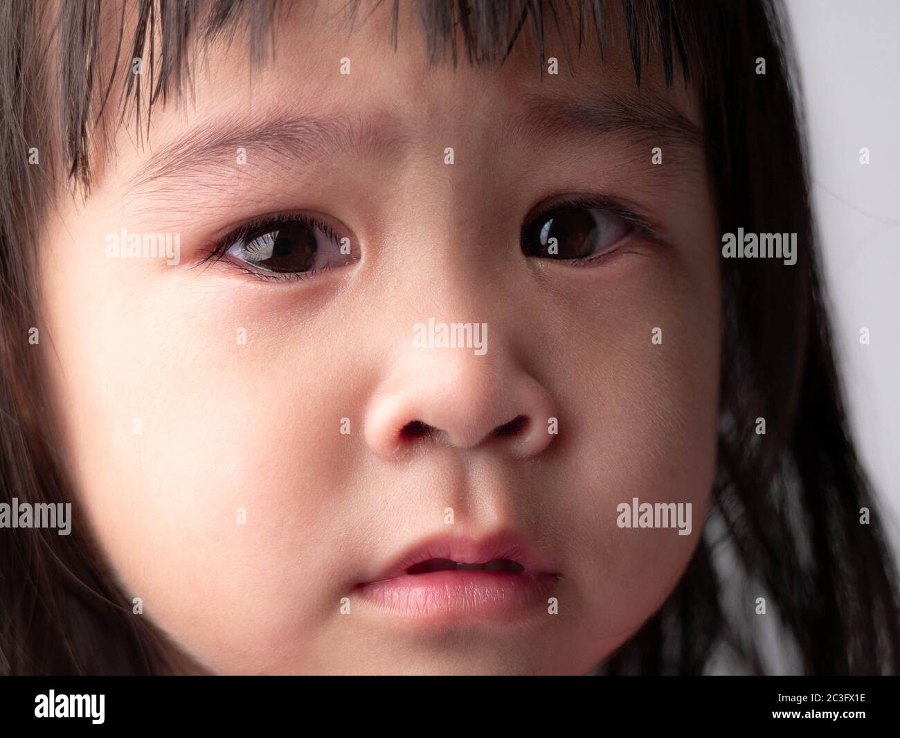 Portrait face of Asian little child girl with sad expression on dark background. Stock Photo