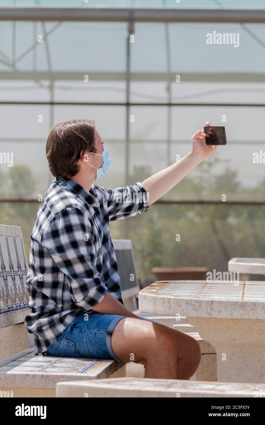 Young man wearing a surgical mask sitting at a table and taking a photo ...