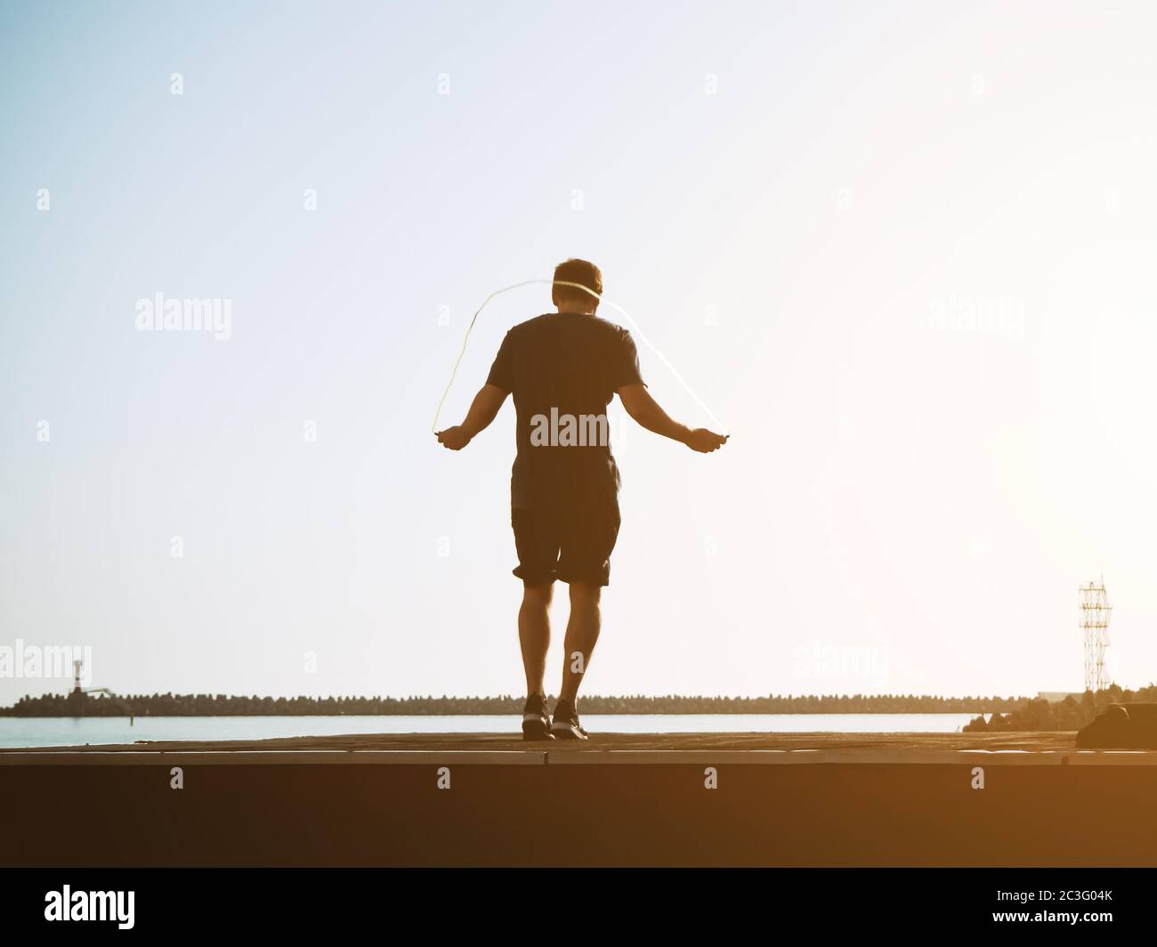 Young guy in shorts jumps on a rope on a sunny day on backgraund sky. Artistic effect. Blurred image Stock Photo