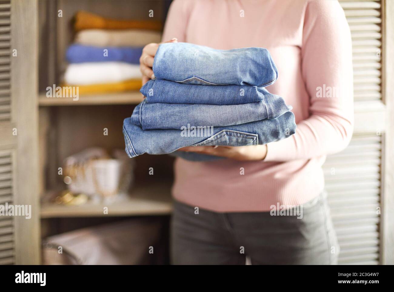 Young shopkeeper woman holding pile of jeans over light background in her hands Stock Photo