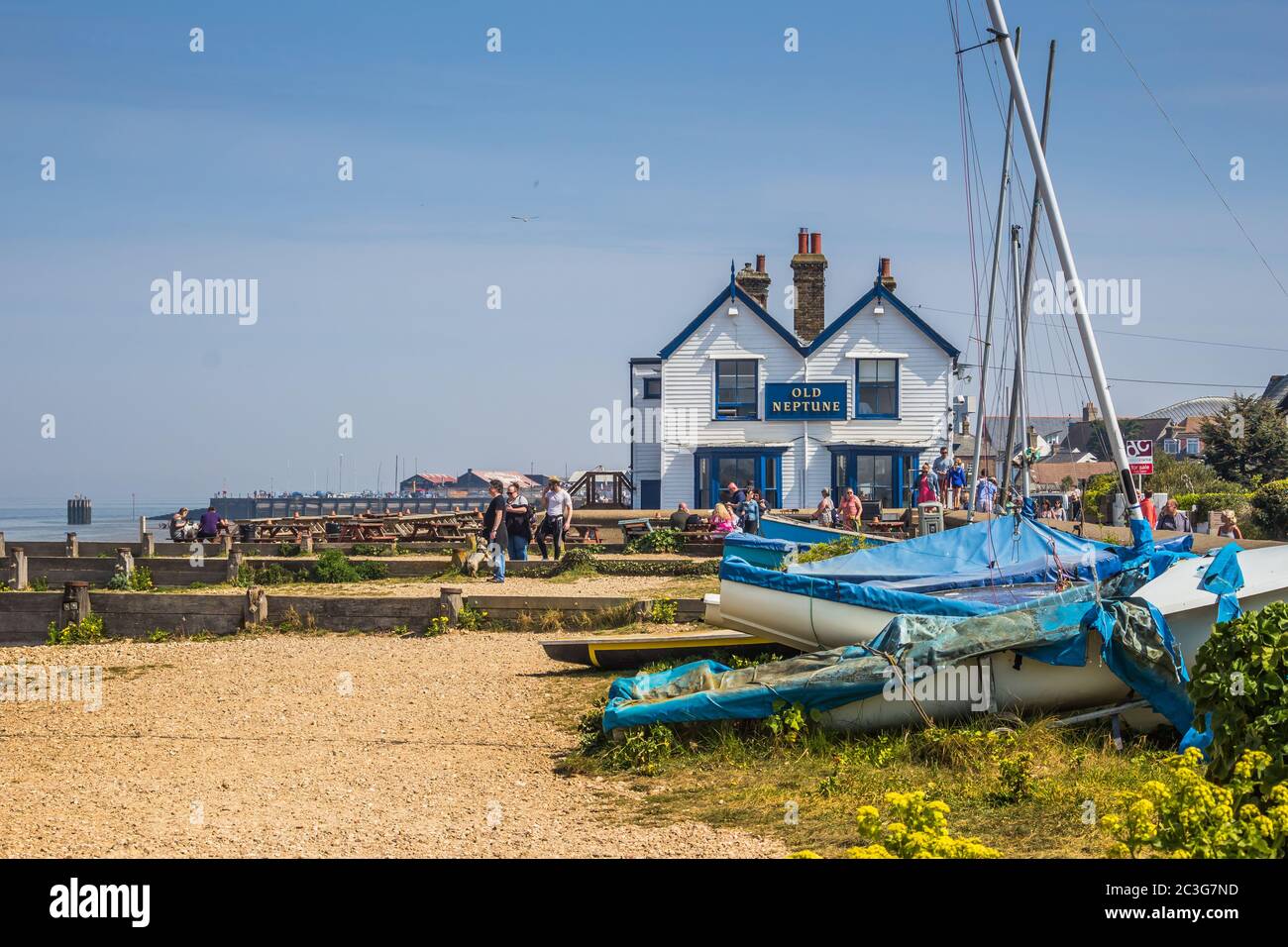 Beach scene with seaside pub, people walking along the beach and old wooden boats in the foreground. Taken in Whitstable Bay on a sunny weekend. Stock Photo