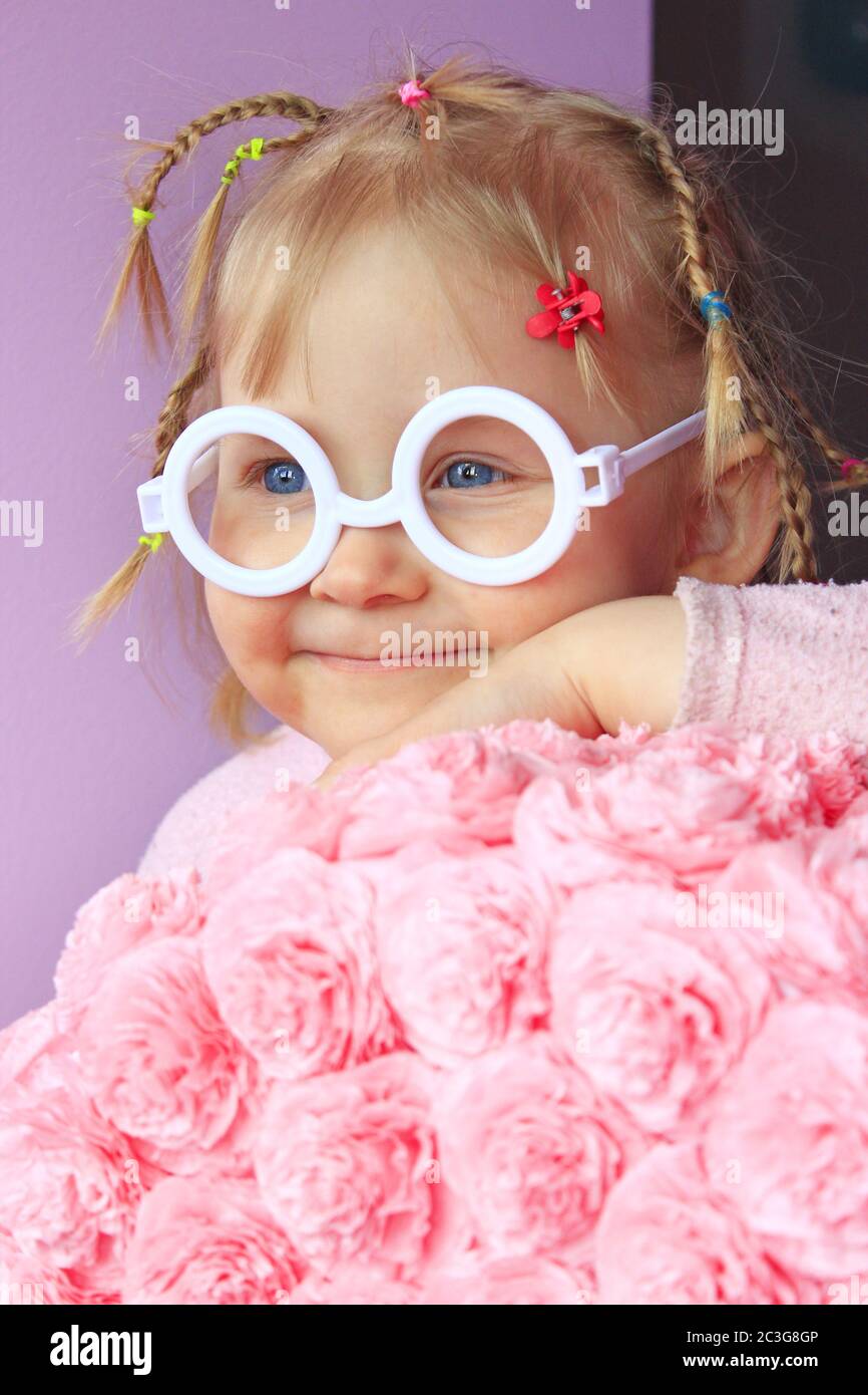 Little girl in plastic glasses smile near paper flowers made from papier-mache. Portrait of baby wit Stock Photo