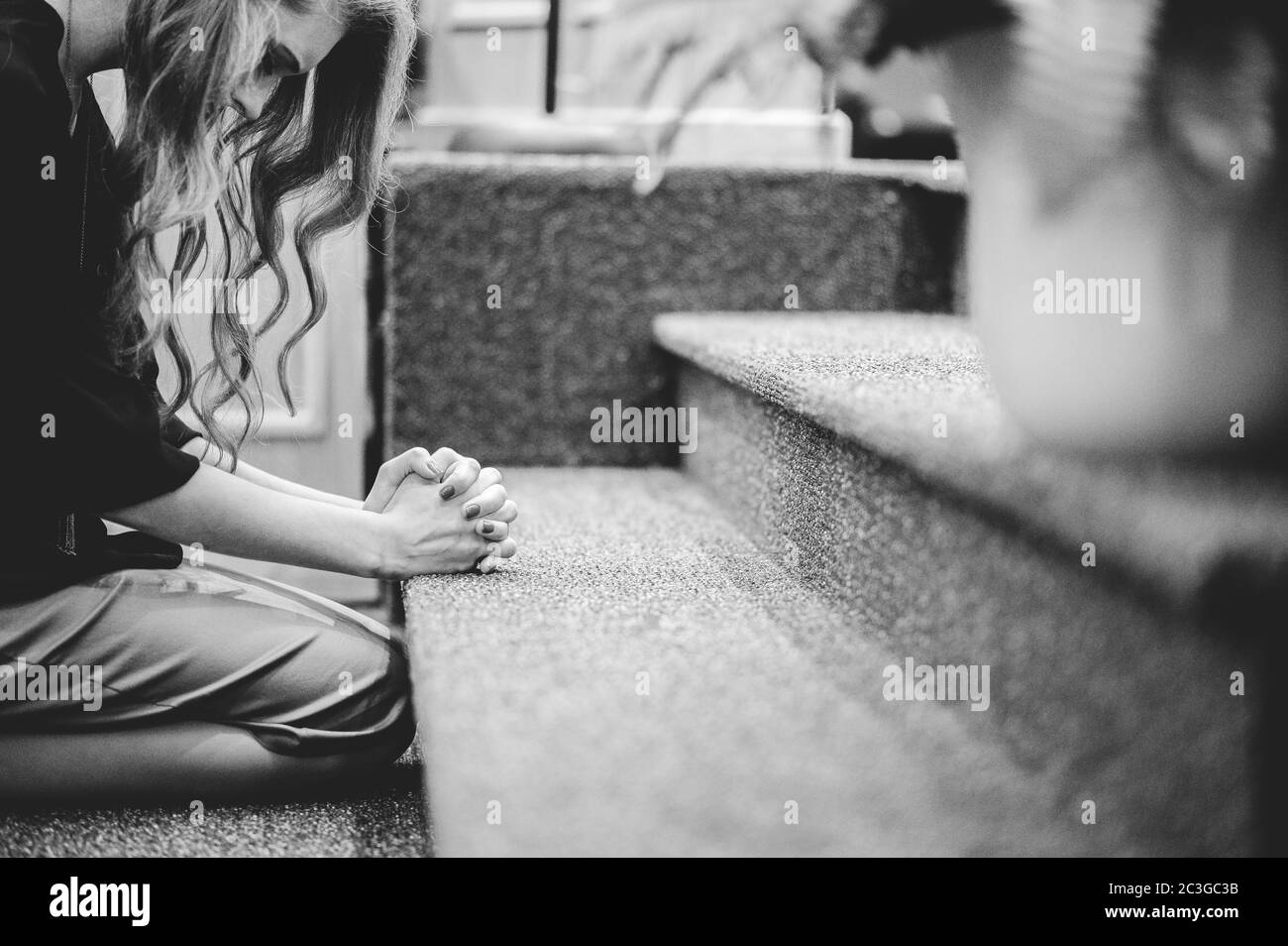 Woman at the front of a church kneeling down and praying Stock Photo