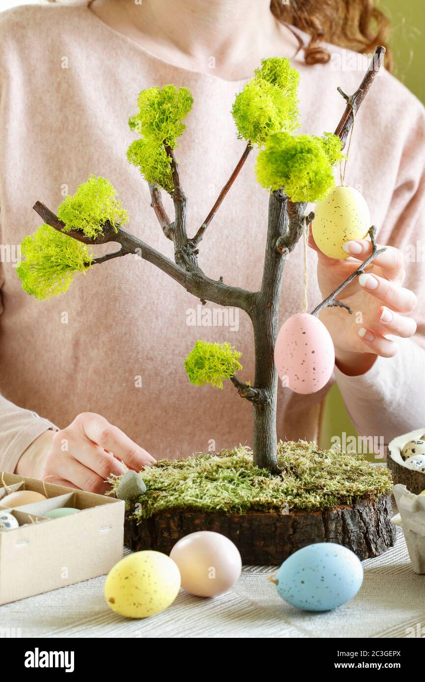 Florist at work: woman shows how to make Easter decoration in tree shape with hanging eggs. Step by step, tutorial. Stock Photo