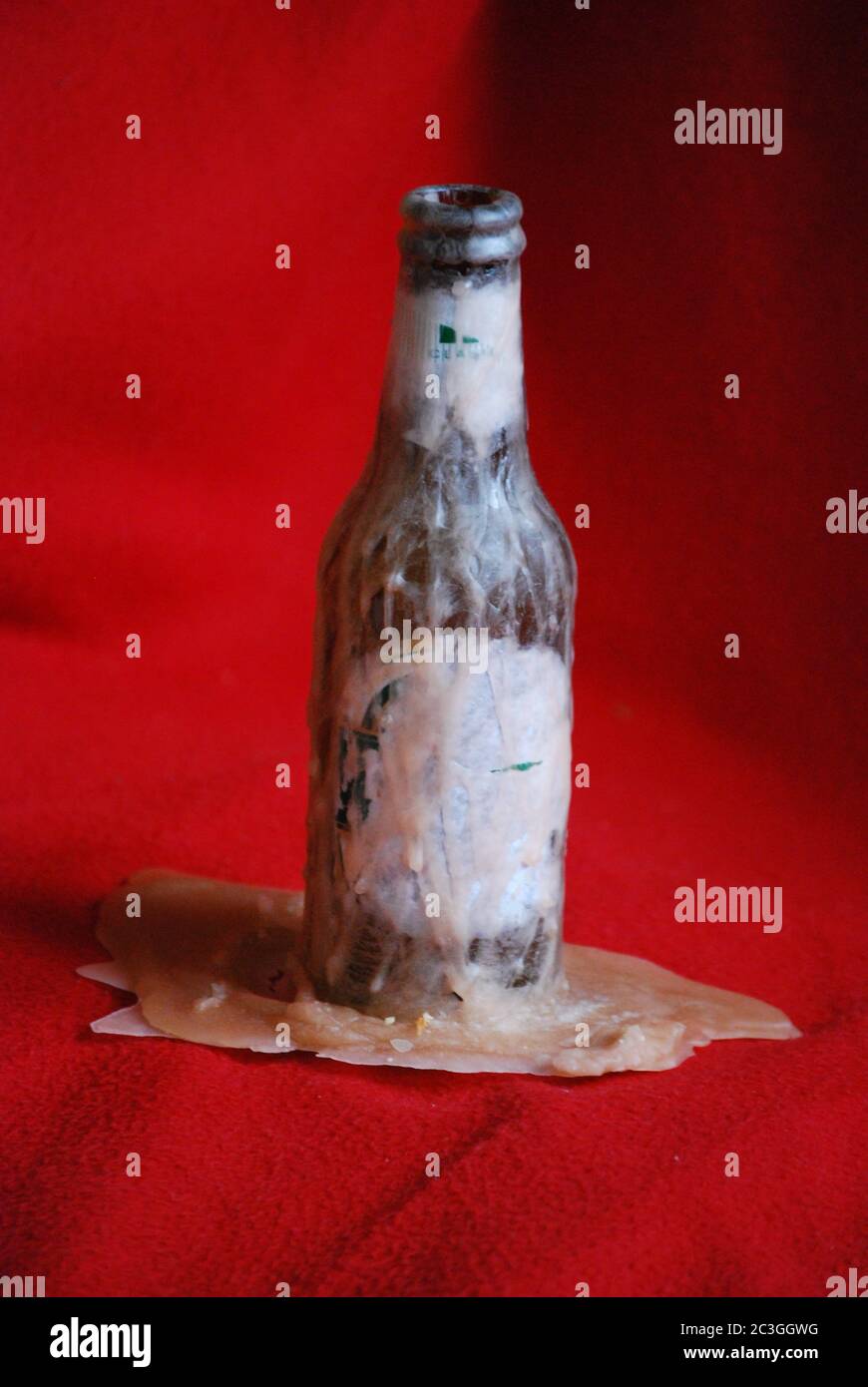 Glass bottle with melted wax flowing from the bottle on a red