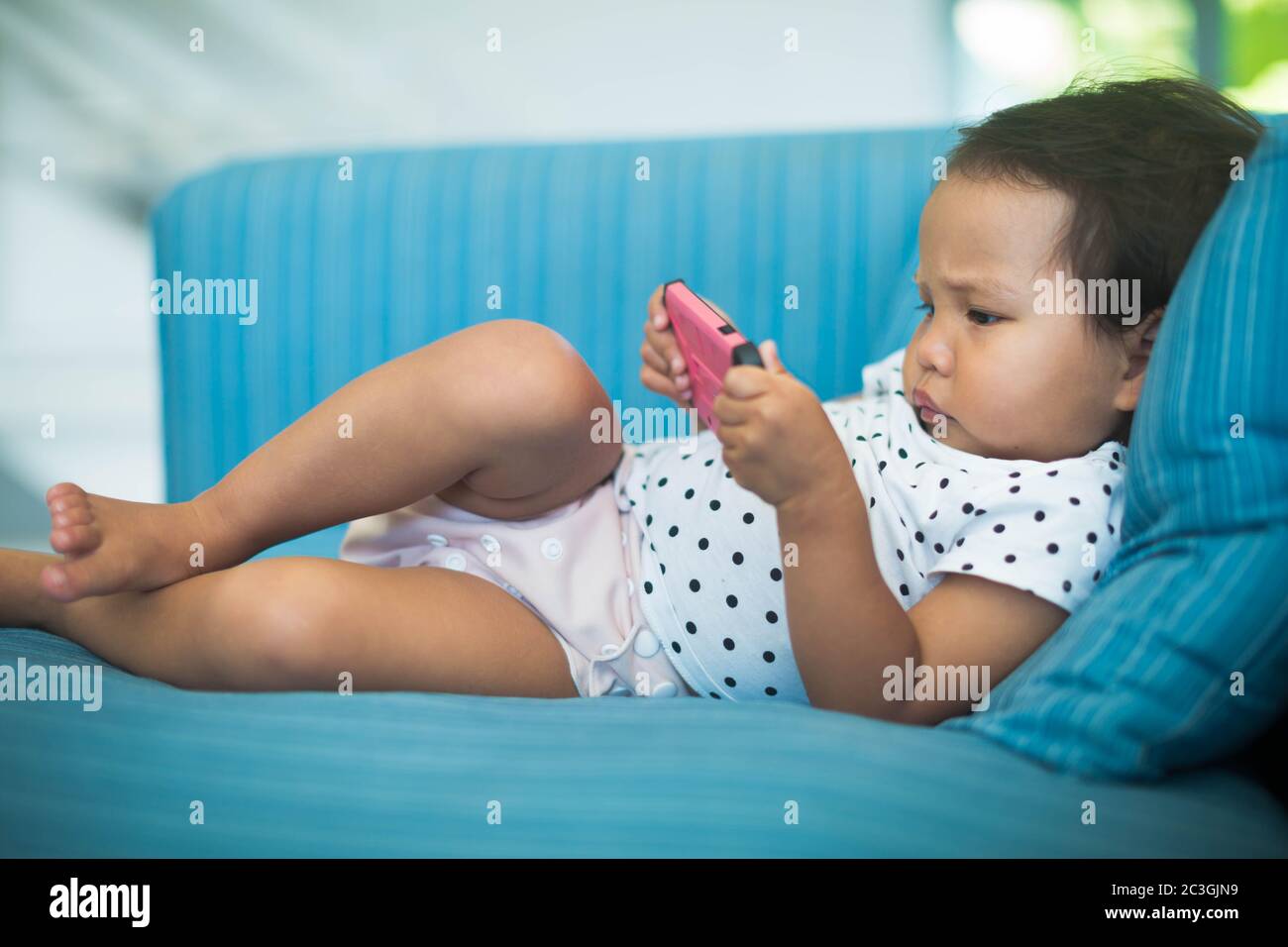 Chubby baby using a pink cell phone by herself on the sofa. High quality photo Stock Photo