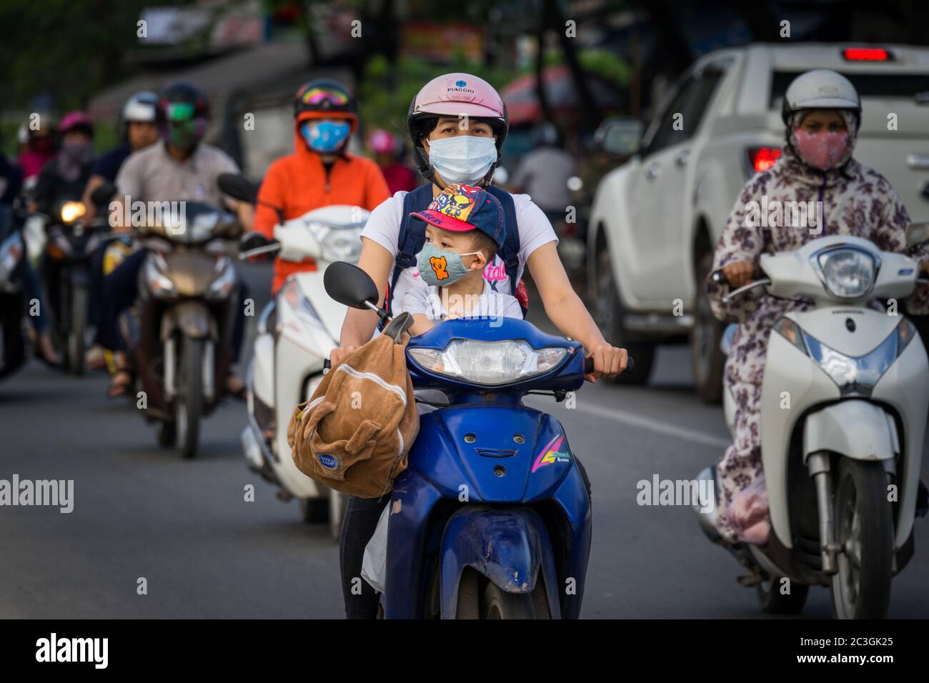 HUE, VIETNAM - Mar 07, 2018: HUE, VIETNAM - MARCH 07, 2018: Woman carrying a child while wearing face mask and riding motorbike on Pham Van Dong stree Stock Photo