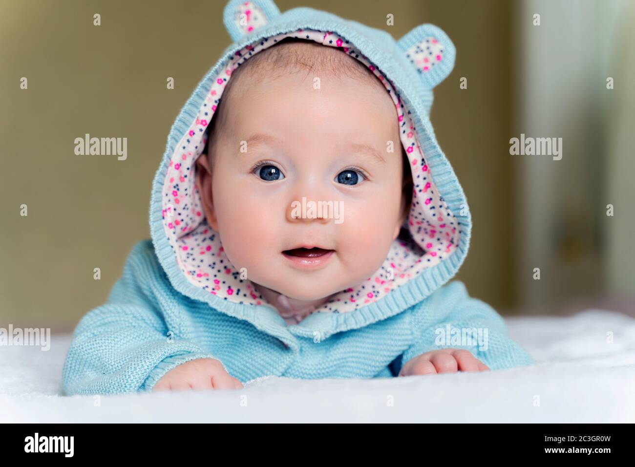 a beautiful newborn blue eyed girl lies on her tummy and smiles Stock Photo