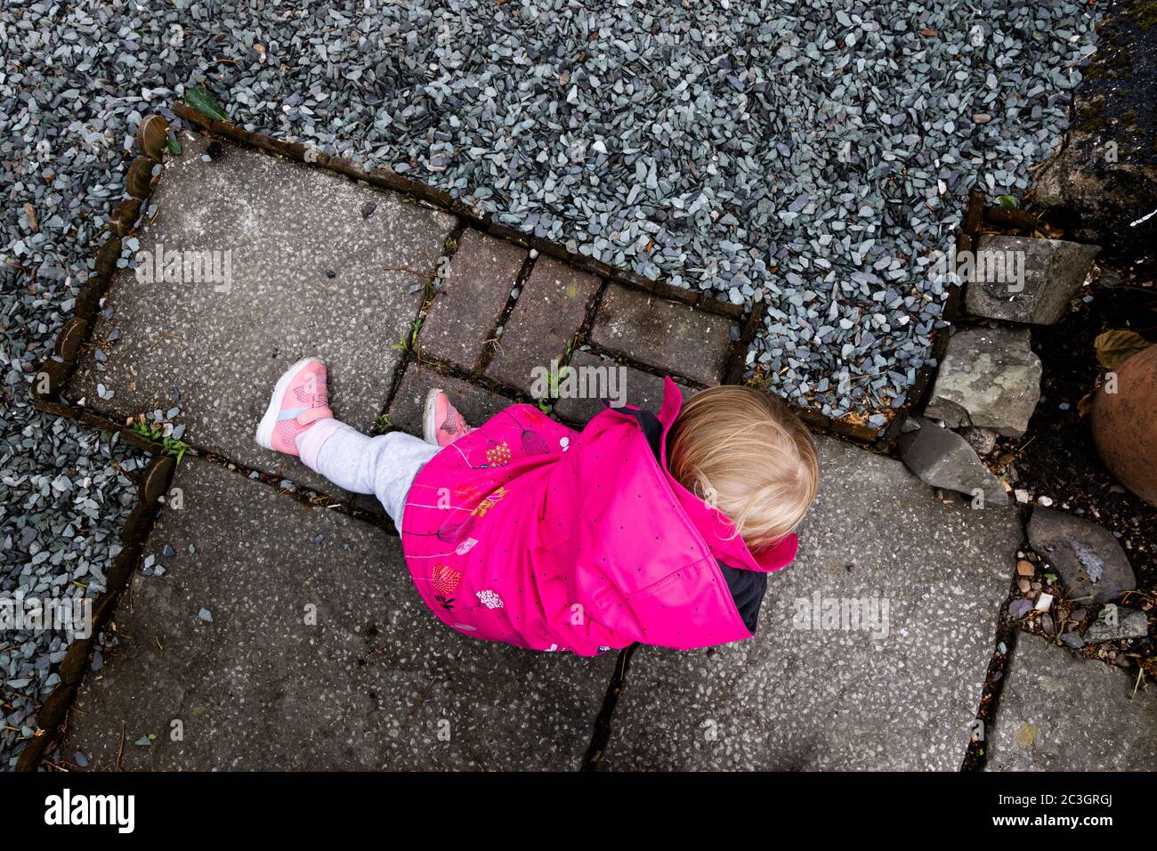 Young child in a pink mac playing on concrete flags, in lock-down isolation, on her own. Stock Photo