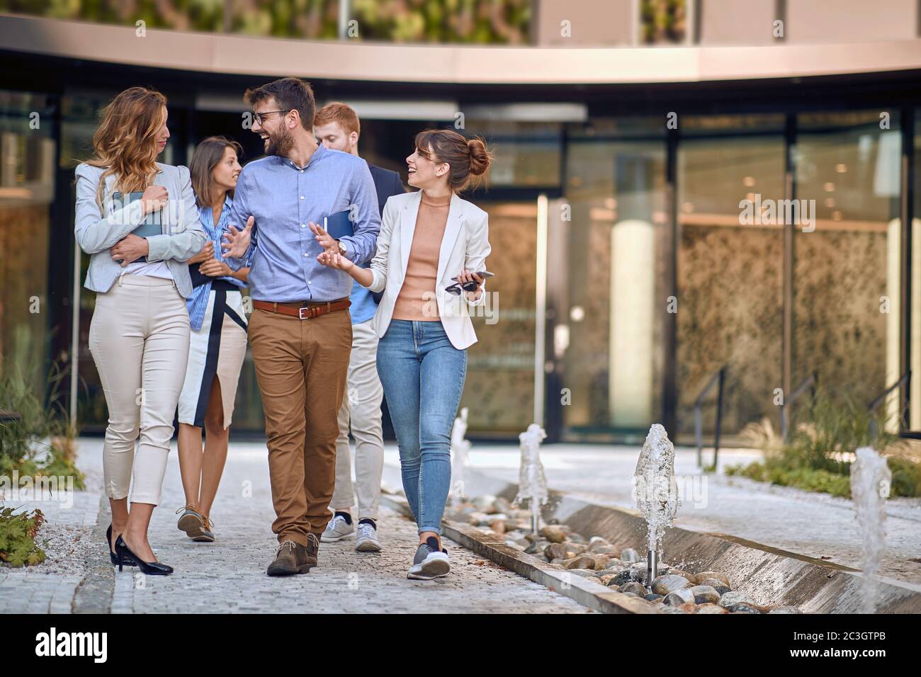 group of colleagues  walking, talking, laughing, in front of business building Stock Photo