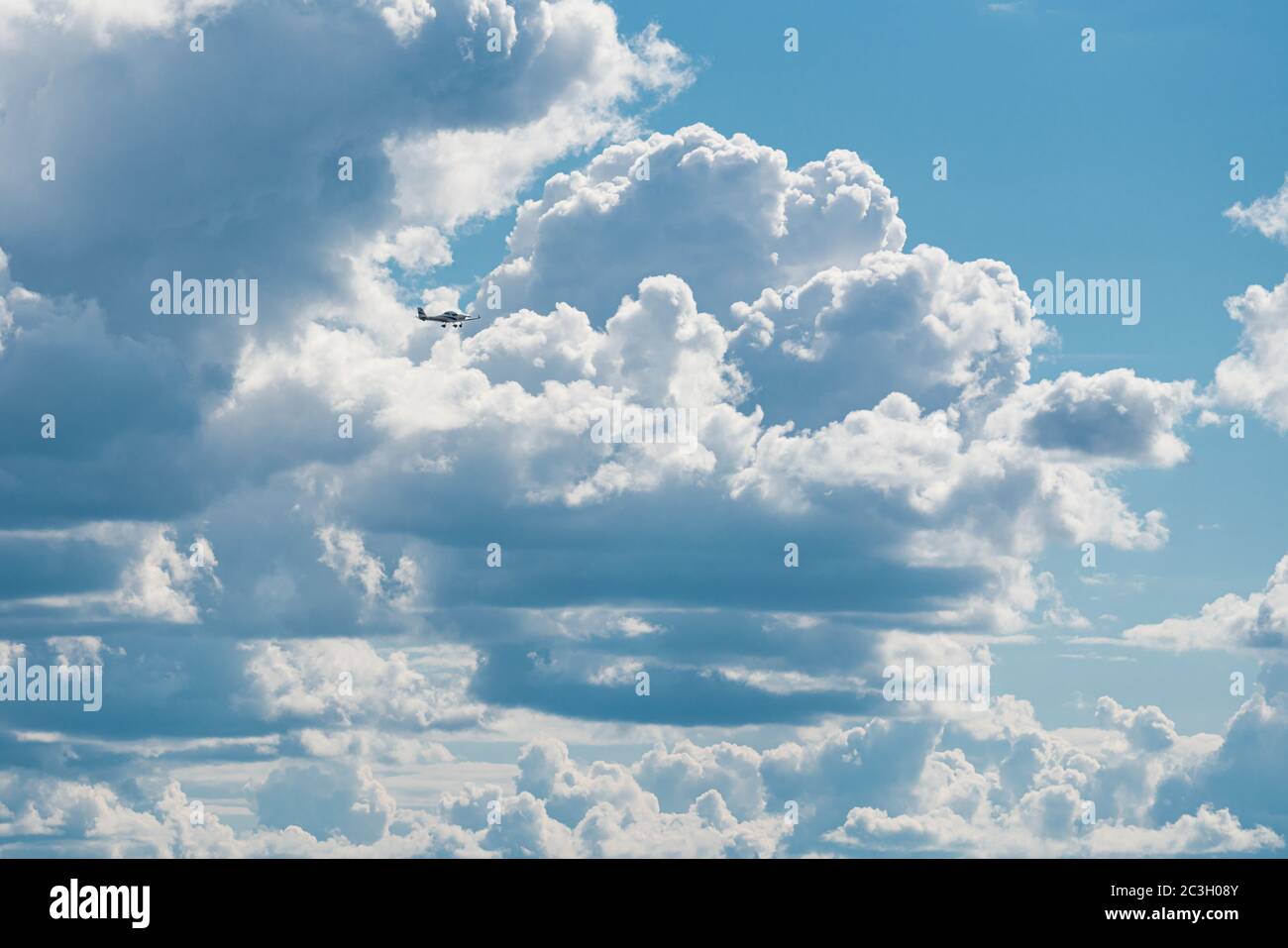 A small motor plane in front of giant clouds after the storm. The clouds break open and blue sky appears. Stock Photo