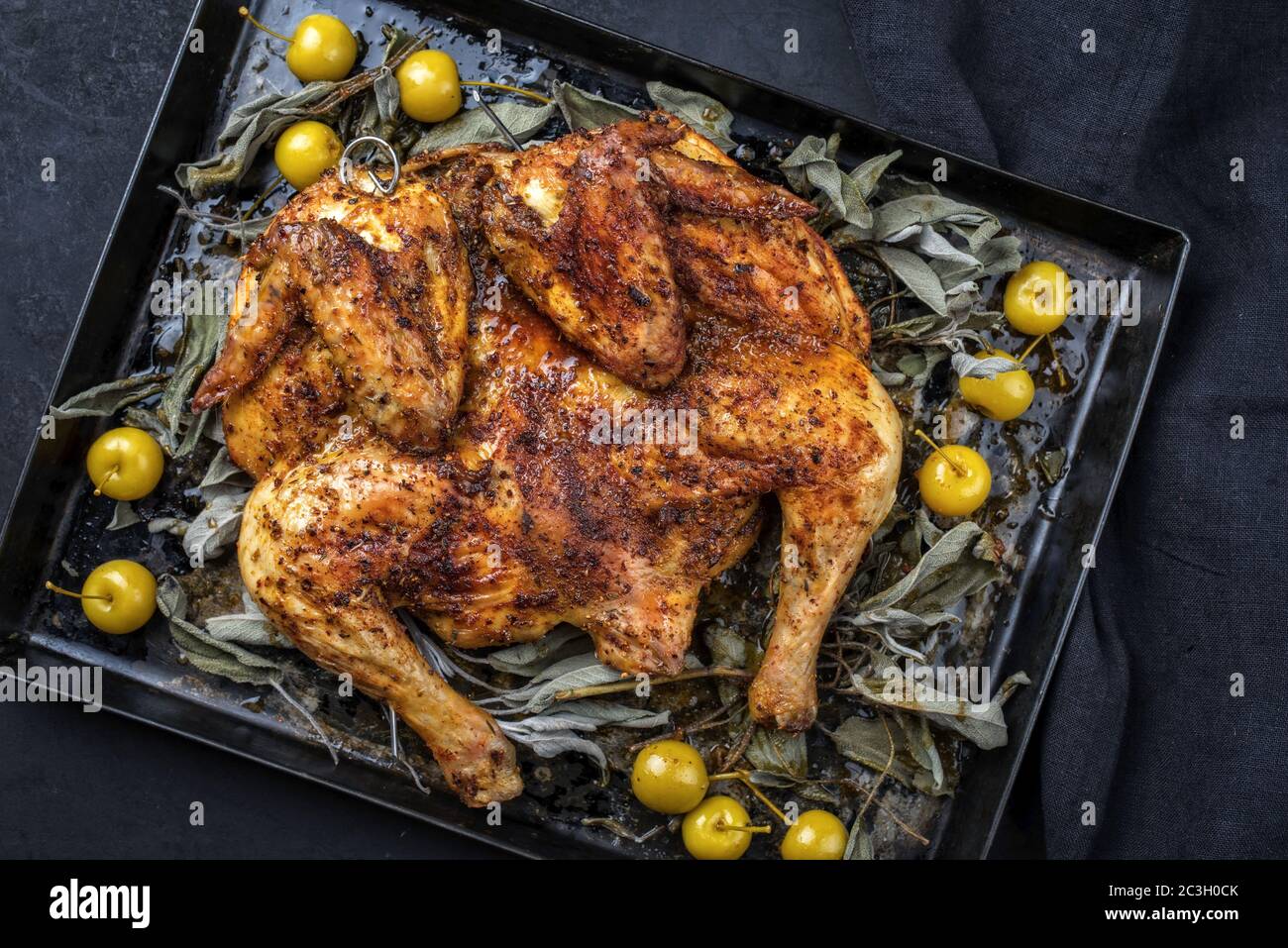 Barbecue spatchcocked chicken al mattone chili with mini apples and sage leaves as top view on an old metal tray Stock Photo