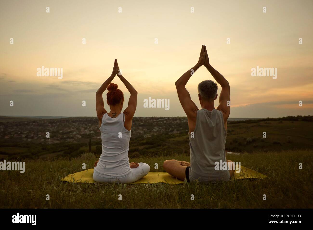 Couple meditating yoga sitting in lotus pose on the nature at dawn. Stock Photo