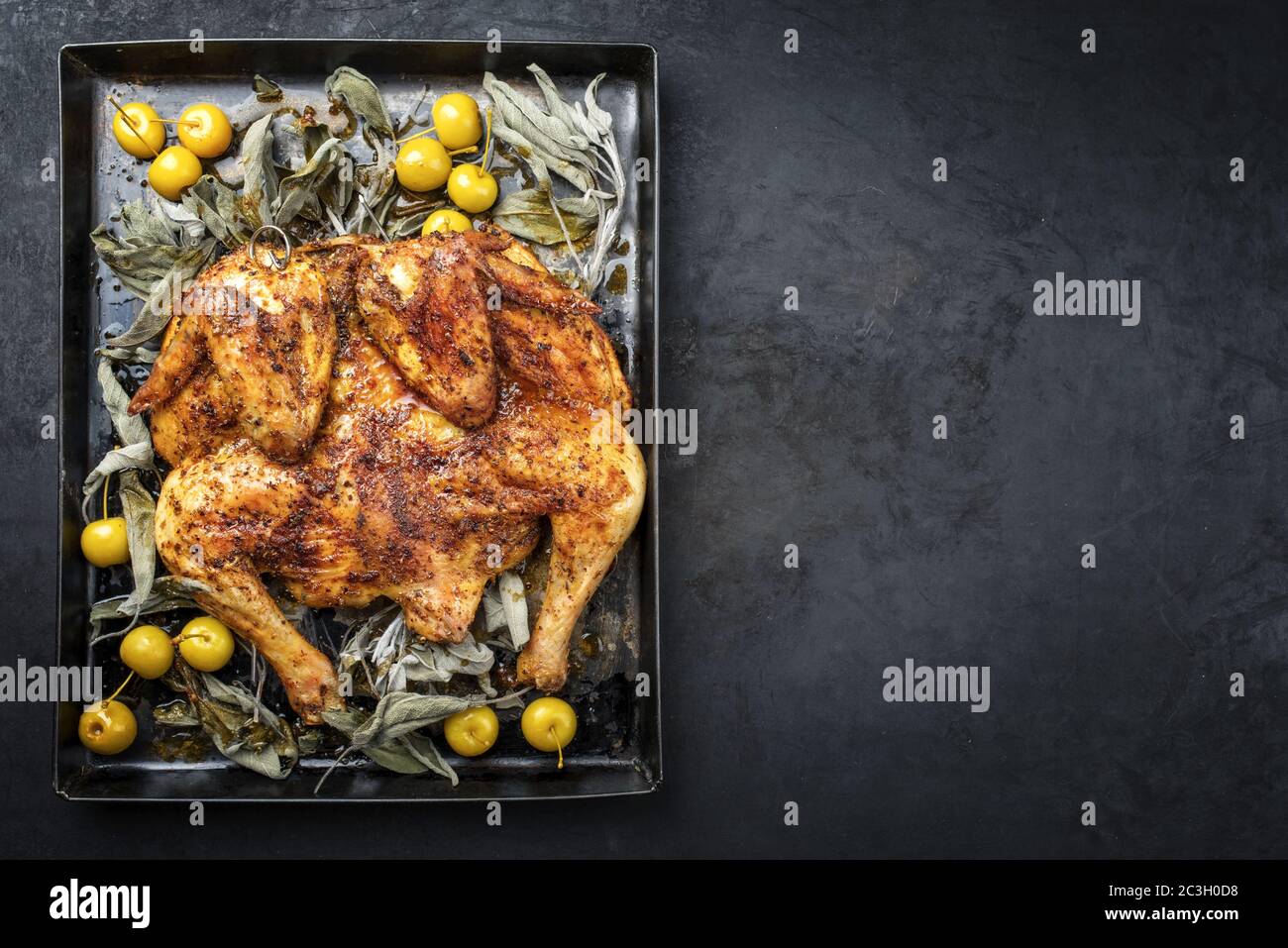 Barbecue spatchcocked chicken al mattone chili with mini apples and sage leaves as top view on an old metal tray with copy space Stock Photo