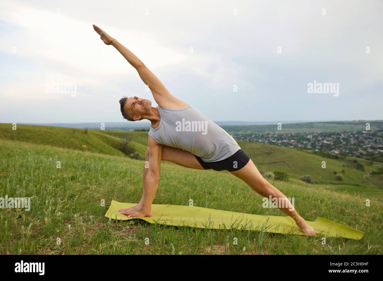 A man practices balance yoga exercises on green grass in nature. Stock Photo