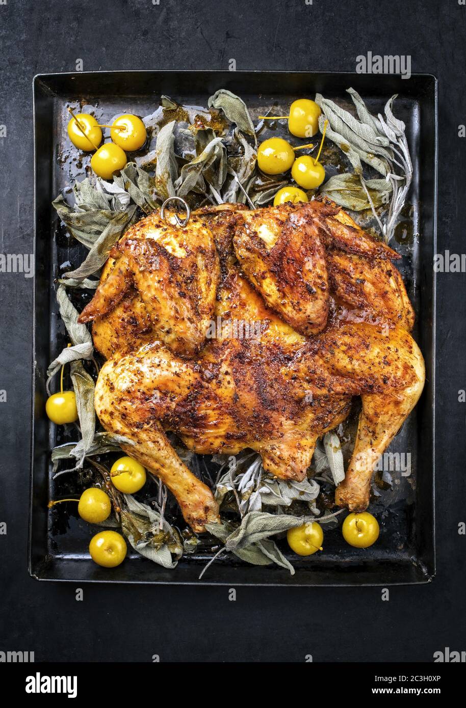 Barbecue spatchcocked chicken al mattone chili with mini apples and sage leaves as top view on an old metal tray Stock Photo
