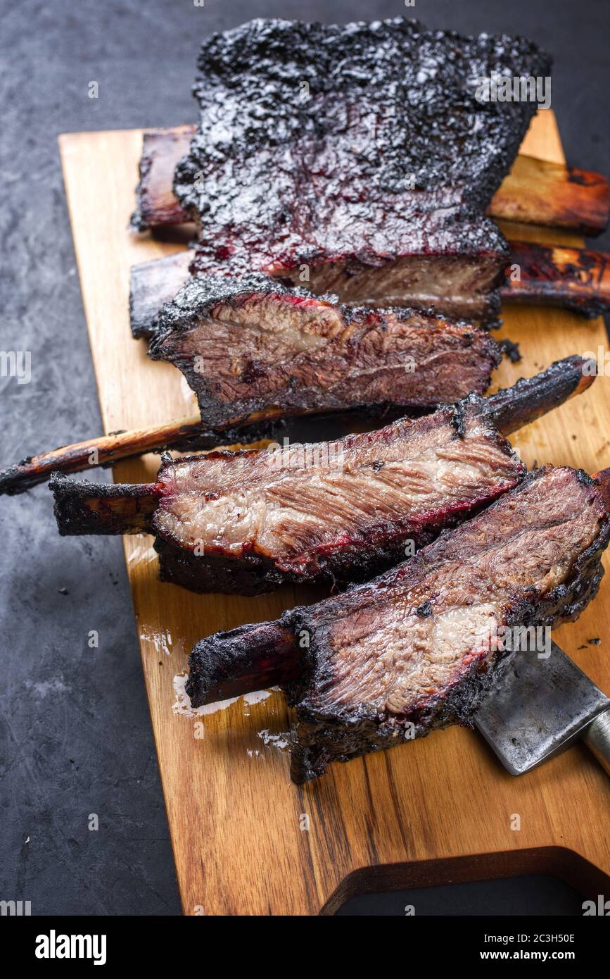 Barbecue burnt chuck beef ribs marinated and sliced as closeup on a modern design wooden board