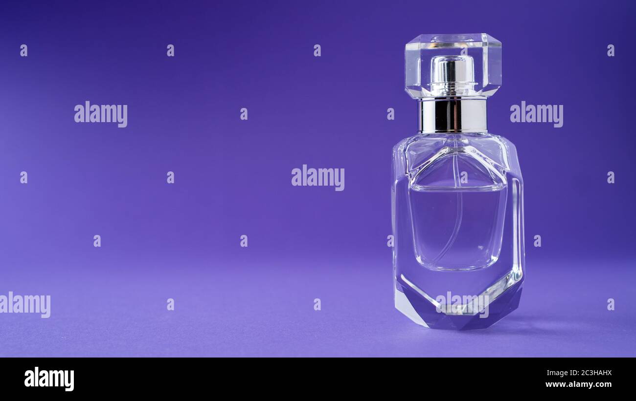 Isolated transparent perfume bottle on purple background. Gift concept. Fragrance spray mock up. Spring scent Stock Photo