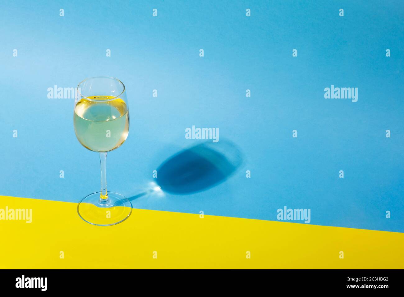Glass of white wine on yellow blue background with long shadow. Shadow effect, hard light. Copy space Stock Photo