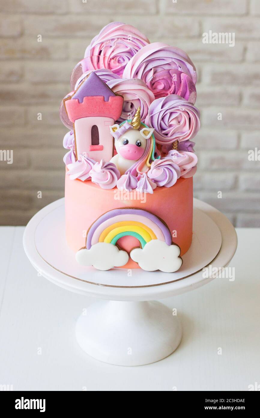 Cute pink birthday cake for a little girl with fondant unicorn, gingerbread princess castle, rainbow and meringue clouds. Stock Photo