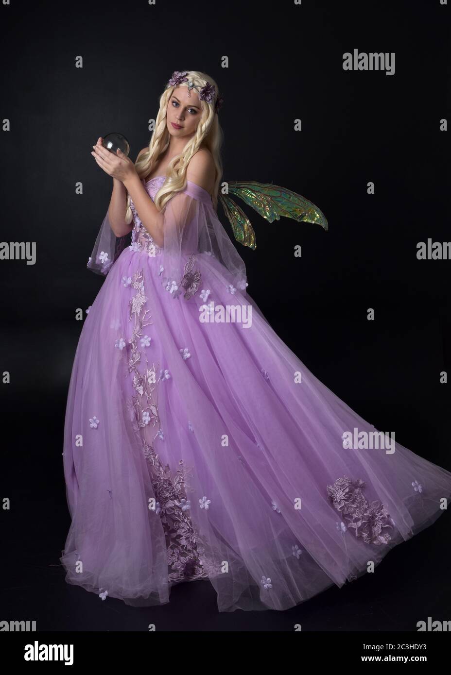 Portrait of a beautiful blonde fairy wearing  purple fantasy gown with wings.  full length standing pose, isolated against a studio background. Stock Photo