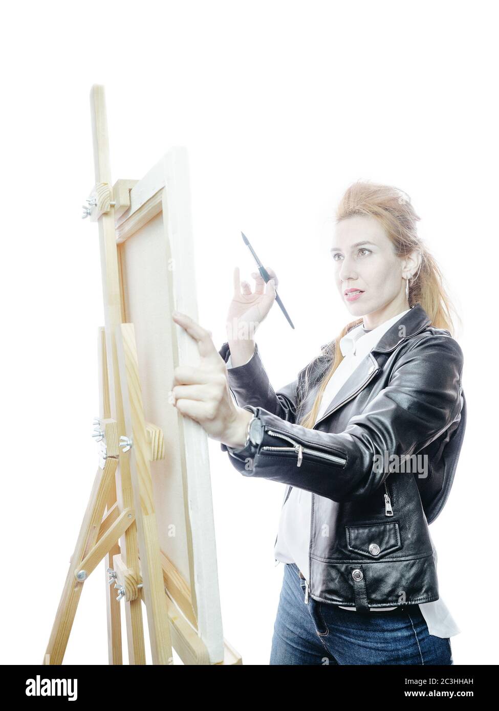 Beautiful girl artist stands in front of easel with a brush on a bright ...
