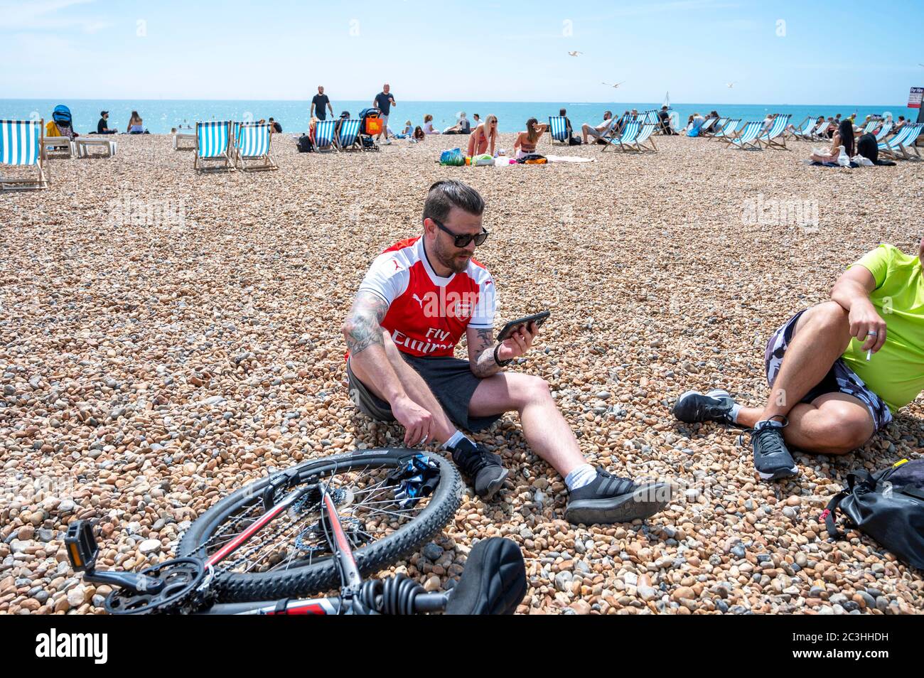 Brighton UK 20th June 2020 -   An Arsenal football fan tunes in his mobile phone on Brighton beach ready to watch the Premier League match against Brighton today during the coronavirus COVID-19 pandemic crisis . All the matches are  being played behind closed doors because of the lockdown restrictions   : Credit Simon Dack / Alamy Live News Stock Photo