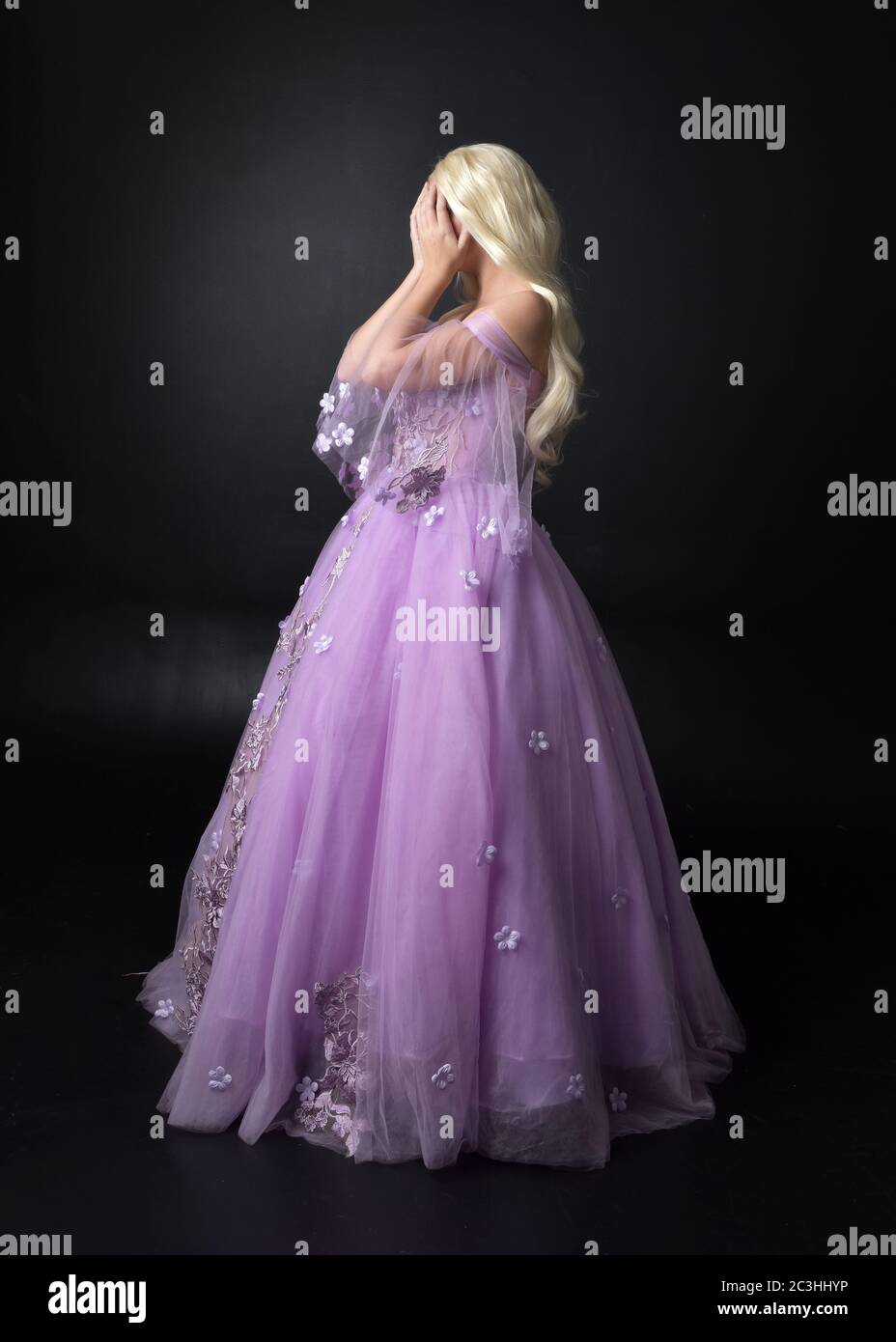 Portrait of a beautiful blonde wearing purple floral, fantasy gown.  full length standing pose, isolated against a studio background. Stock Photo