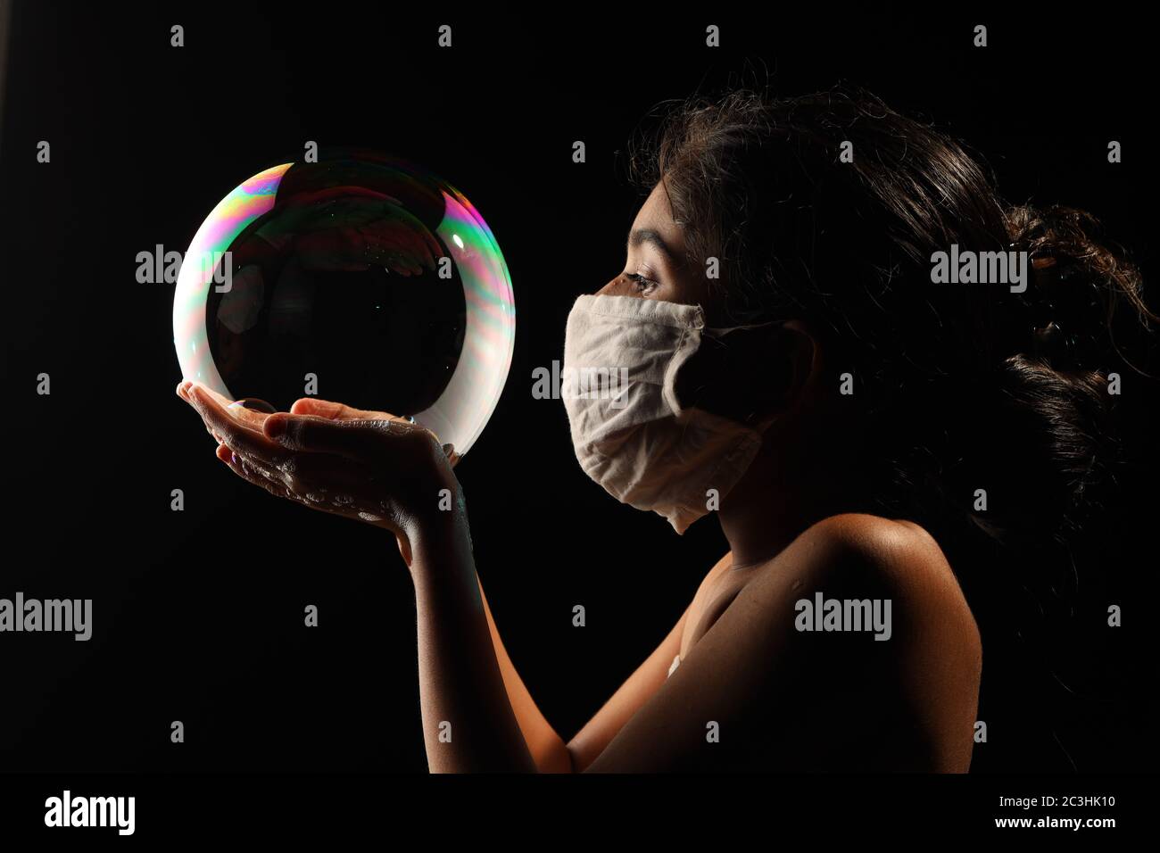 Midshot of a girl catching soap bubble  by wearing mask resemble a kid hopping for COVID free new world. Stock Photo
