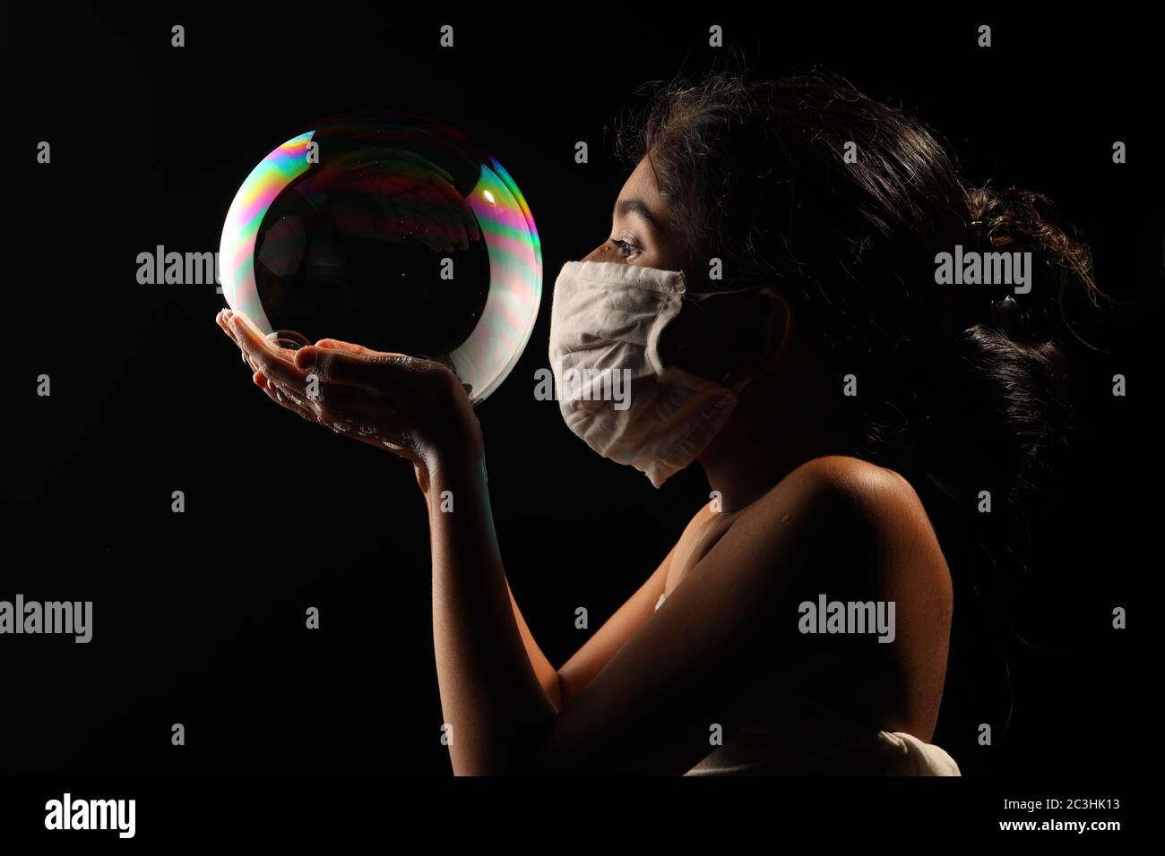 Midshot of a girl catching soap bubble  by wearing mask resemble a kid hopping for COVID free new world. Stock Photo