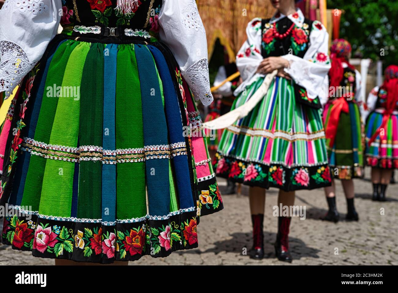 Girls dressed in polish national folk costumes from Lowicz during Corpus Christi procession. Close up of traditional colorful striped folk skirts Stock Photo