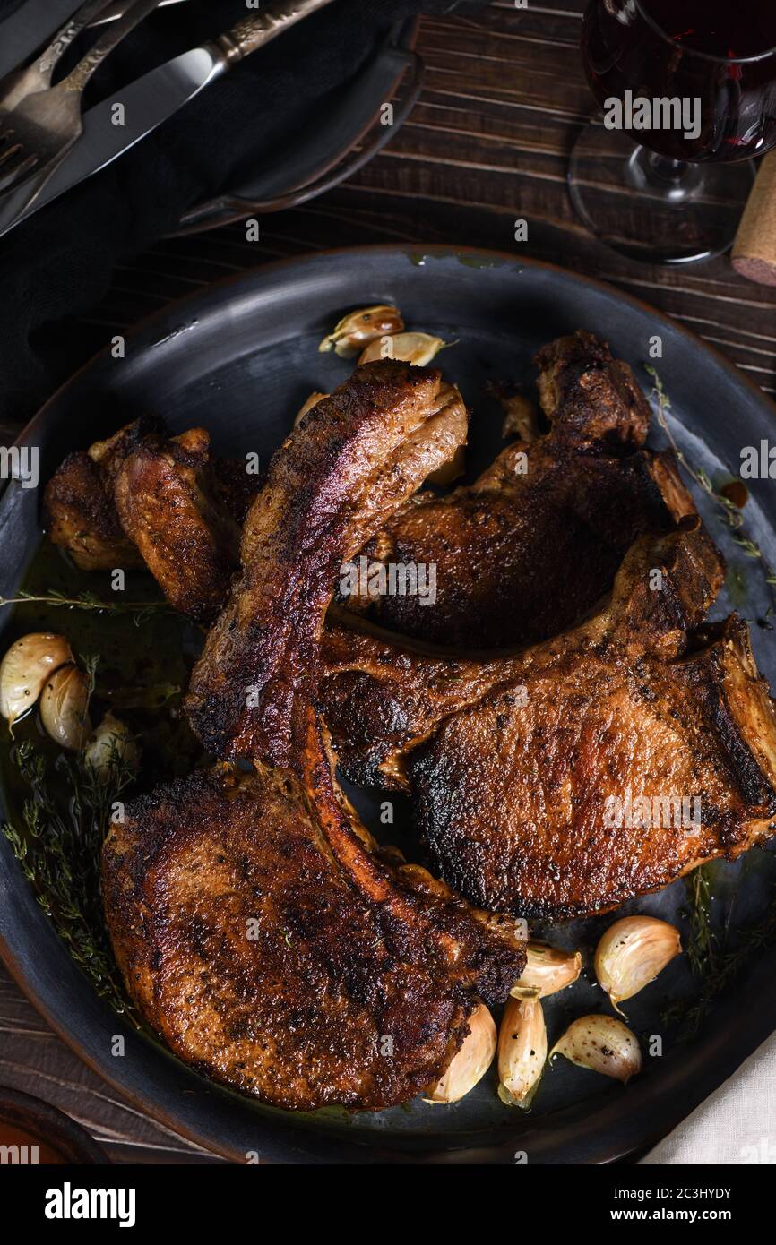 Juicy, slice of fried pork chop on a bone in oil with garlic and herbs in a pan.  Flat lay Stock Photo