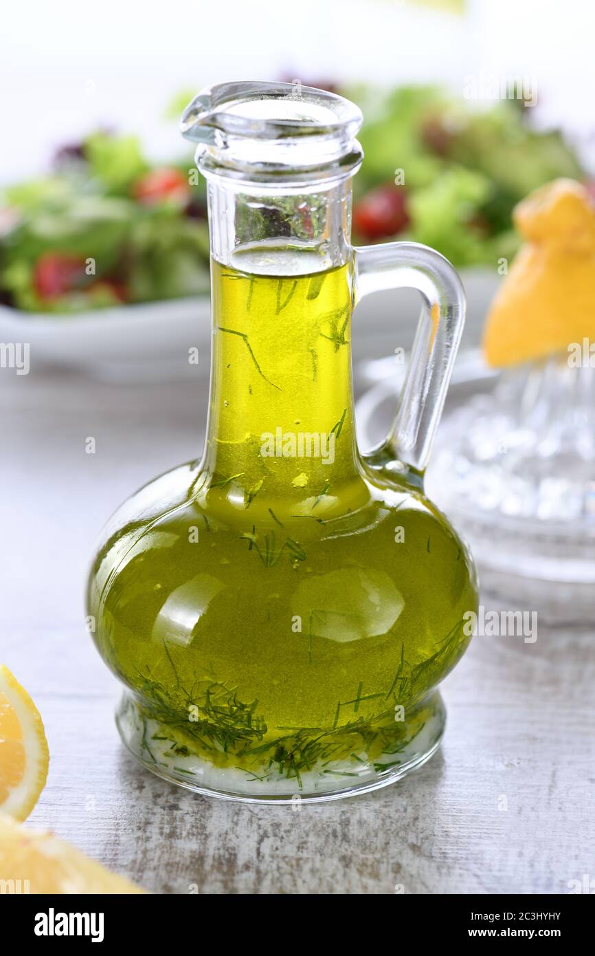 Flavored fresh natural olive oil with herbs and garlic in a glass sauce boat bottle, an ideal salad dressing. Stock Photo