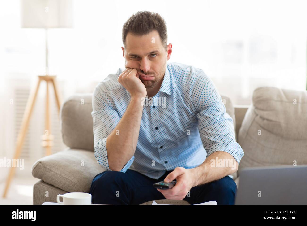 Tired man watching TV at home, holding remote control Stock Photo