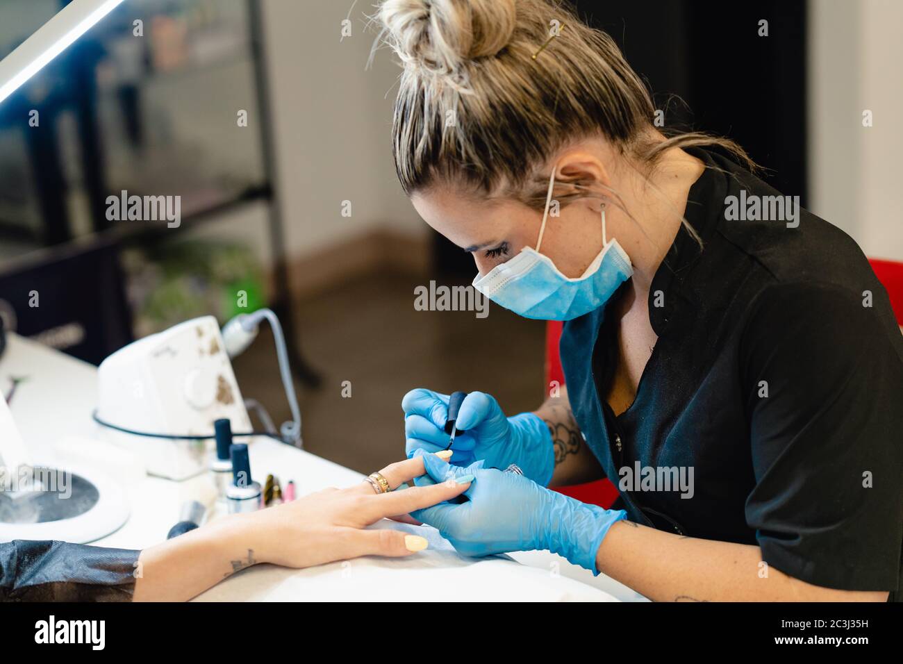 Close-up of Beautician painting her client's nails in blue and yellow nail varnish. Stock Photo