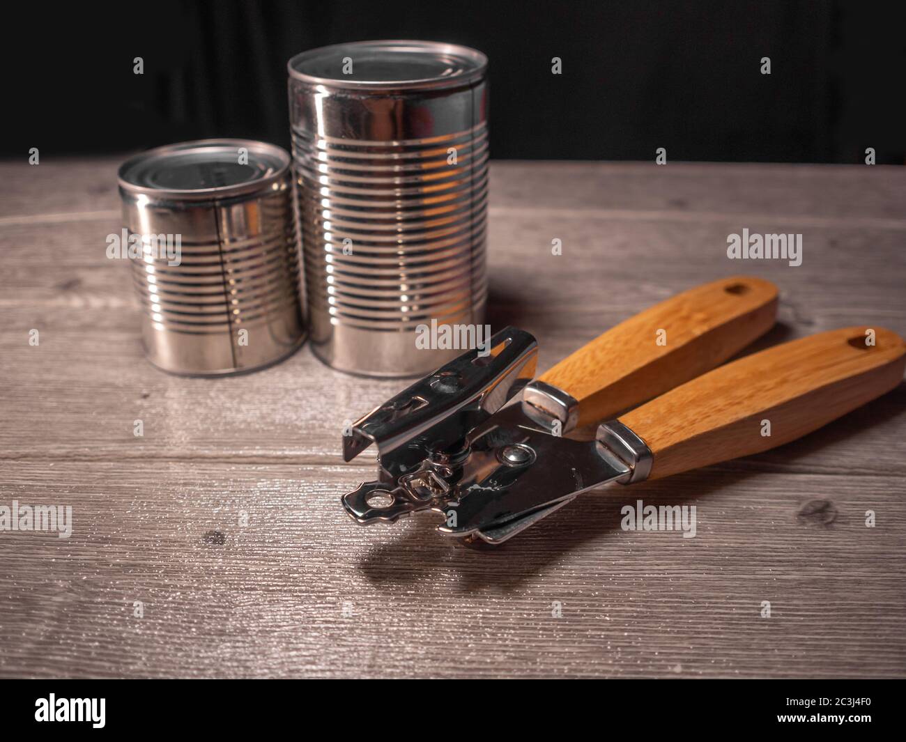 https://c8.alamy.com/comp/2C3J4F0/two-canned-aluminum-products-with-a-stainless-steel-and-wooden-can-opener-a-wooden-board-and-a-black-background-2C3J4F0.jpg