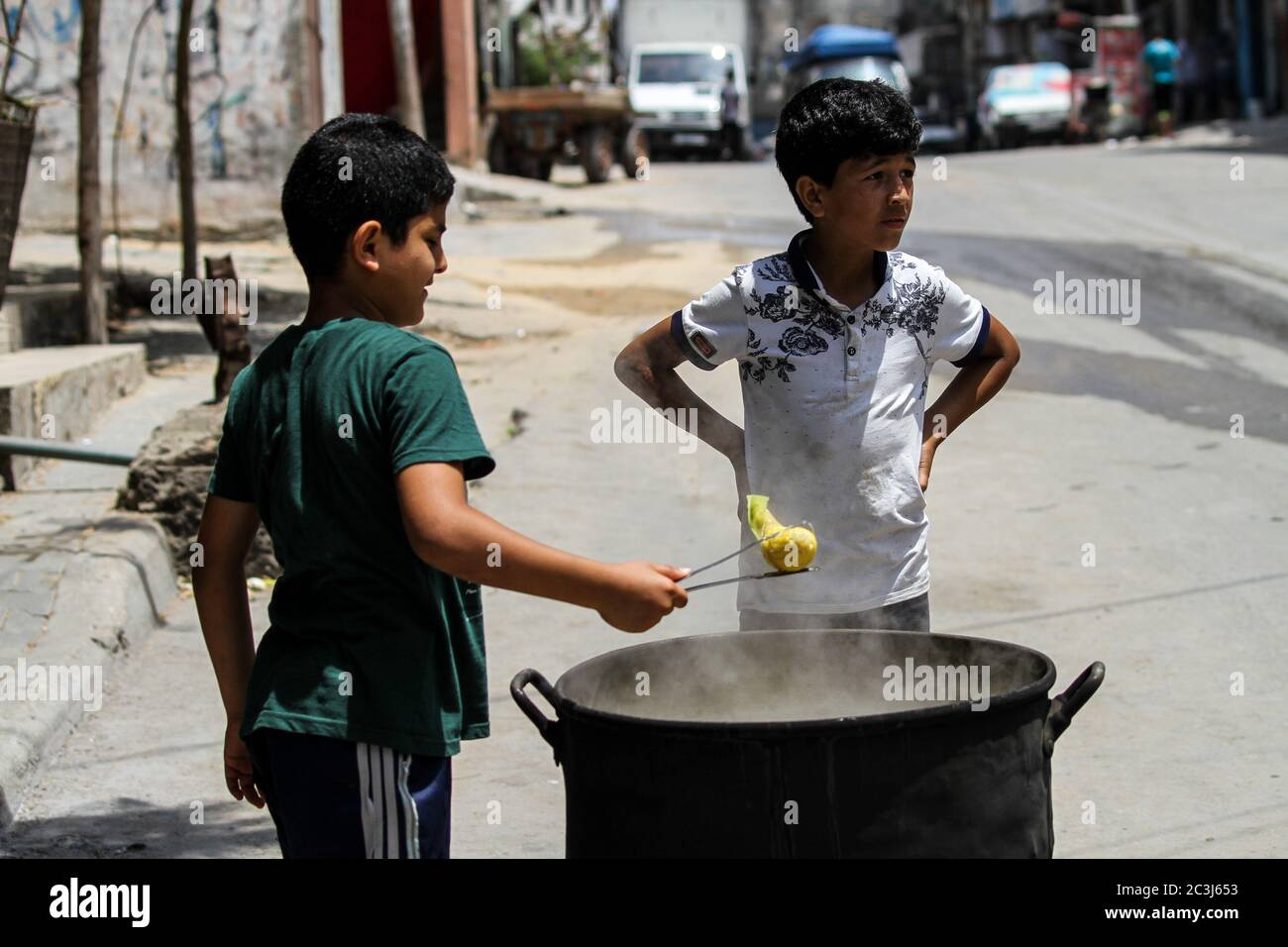 June 20, 2020: Gaza, Palestine. 20 June 2020. A Palestinian child cooks corn on the grill in the Al-Shati refugee camp in the northern Gaza Strip on World Refugee Day. The Al-Shati camp, which was established in 1948 for about 23,000 Palestinians fleeing their towns during the 1948 Arab-Israeli War, is the third largest of the Gaza Strip's eight refugee camps. It extremely overcrowded, lacks in major infrastructures, and has a high unemployment rate, with children sometimes having to work to provide some income to their families. World Refugee Day celebrates refugees' courage and resilien Stock Photo